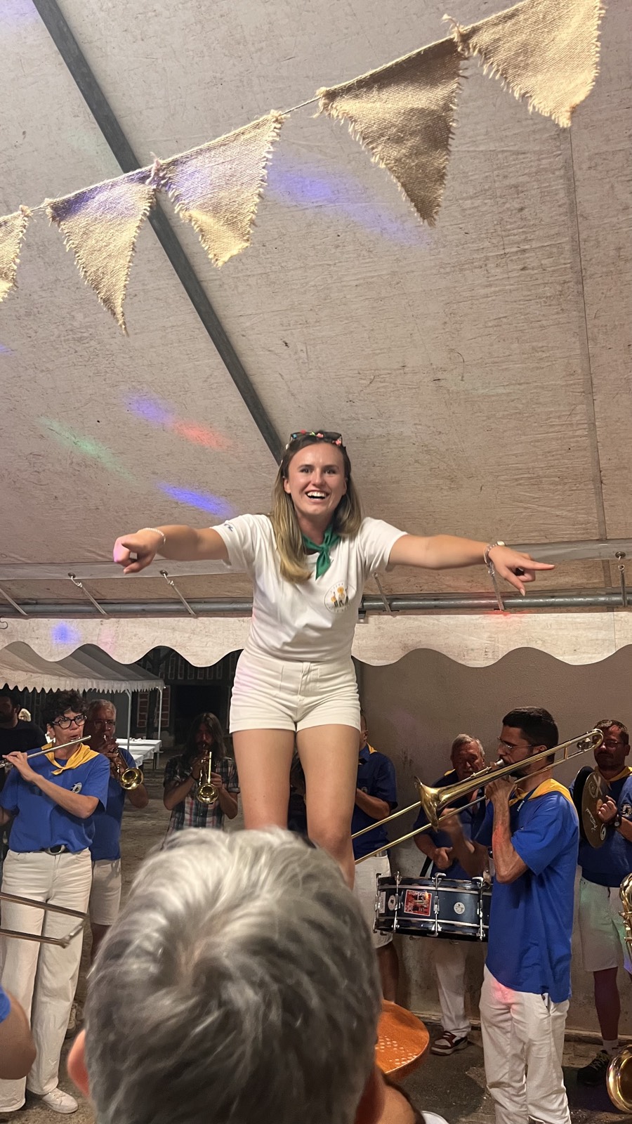 Une jeune femme debout bras écartés devant les musiciens en tenue bleue et jaune d'une banda