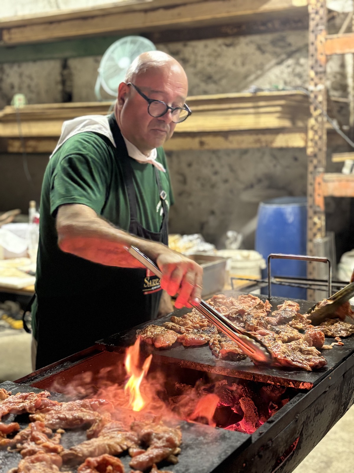 Un cuisinier retourne des grillades à la pince sur une plancha chauffée aux braises