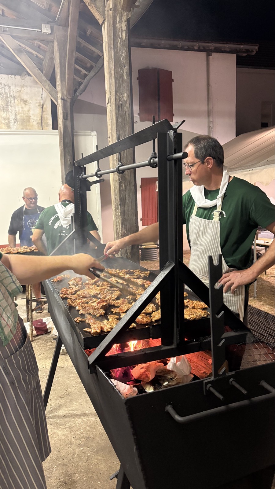 Un cuisinier devant une grande grille de viande au-dessus des braises