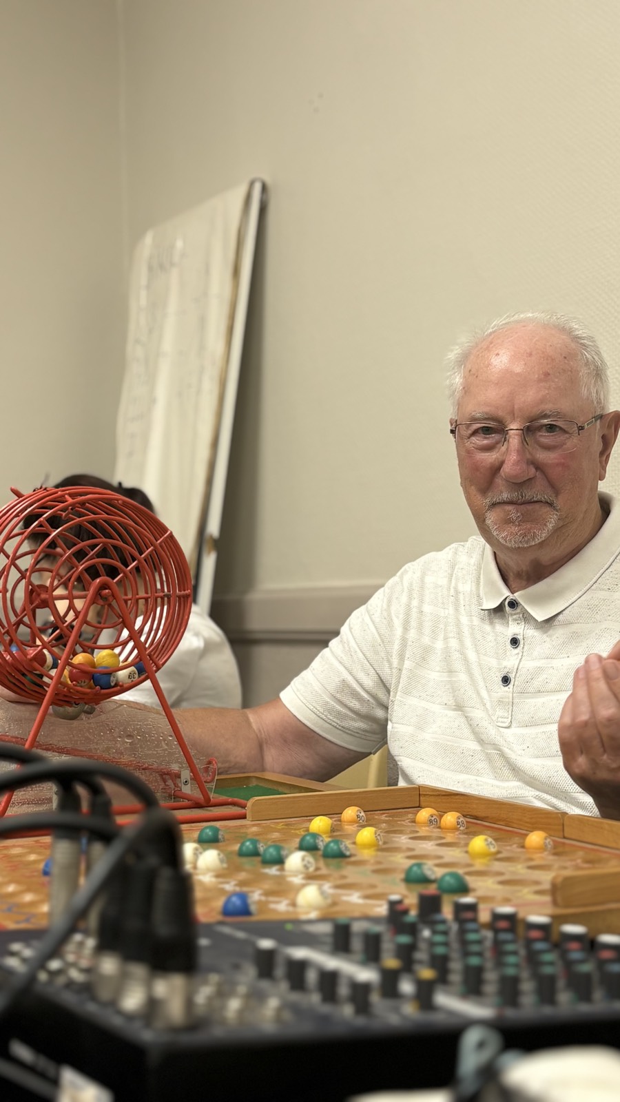 Un animateur devant le boulier rouge du loto, cartons et pions posés sur la table