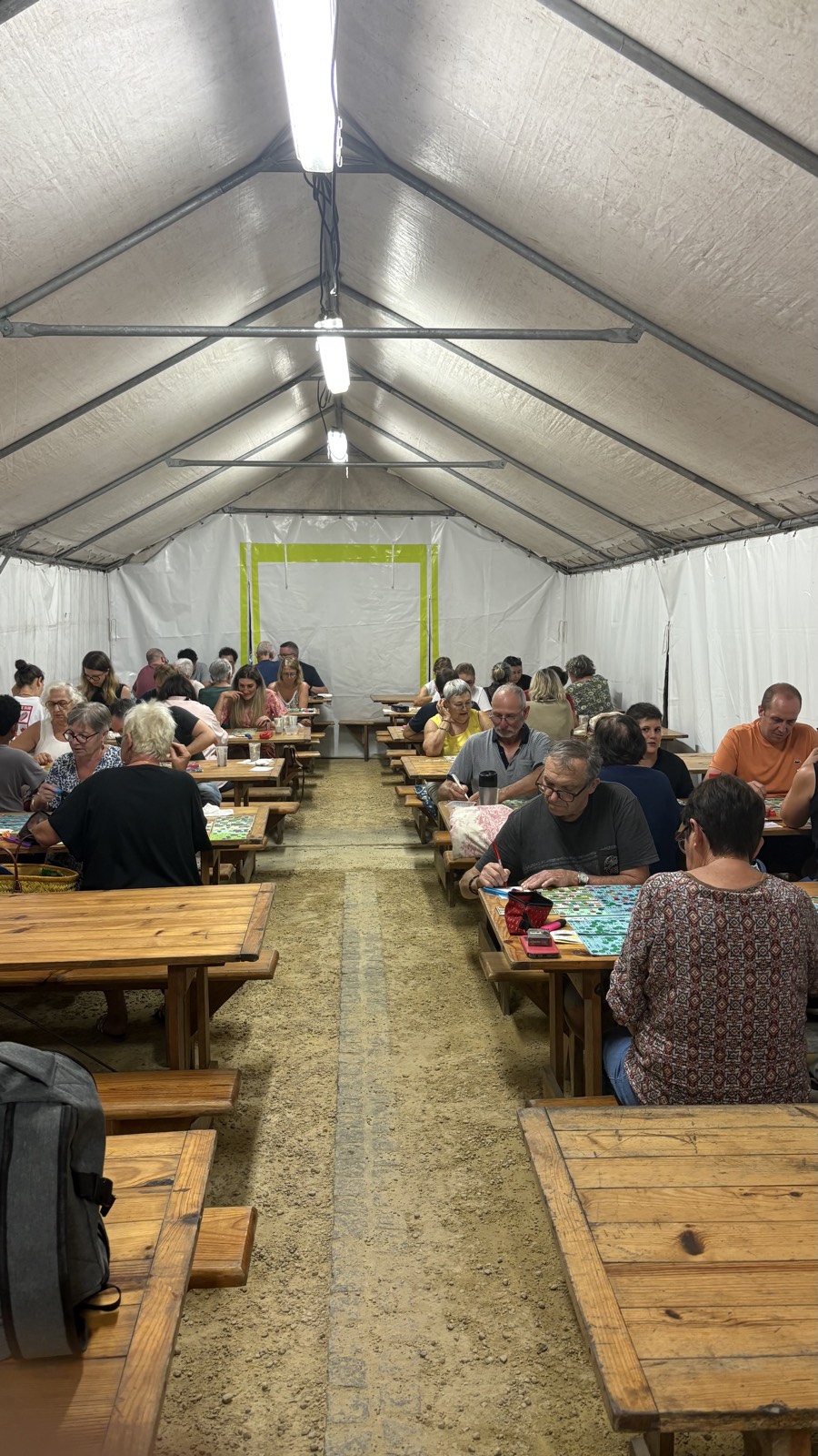 Vue intérieure du chapiteau, tables et bancs de bois occupés par les joueurs de loto