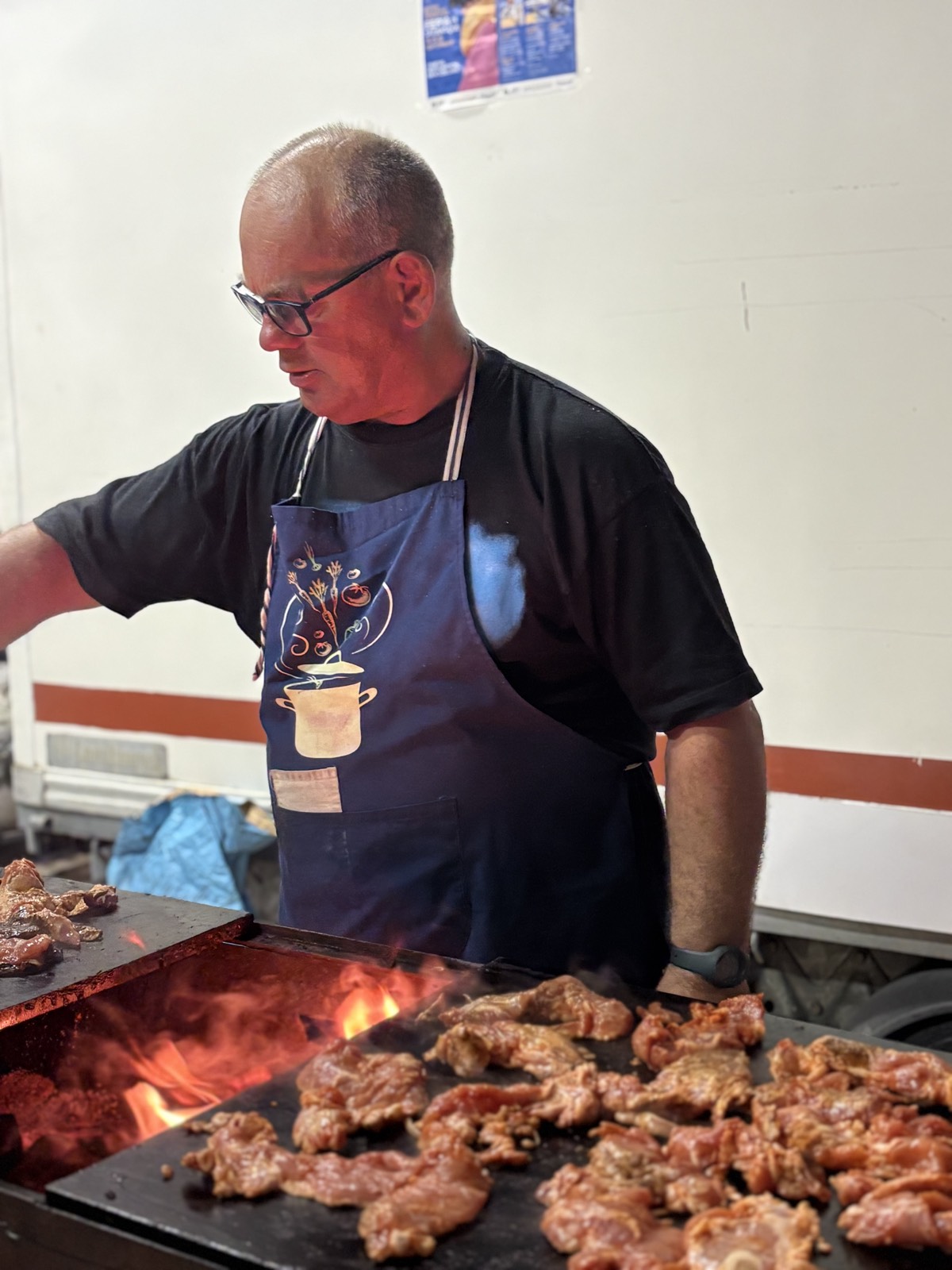 Un cuisinier retourne la viande, les flammes visibles sous la plancha