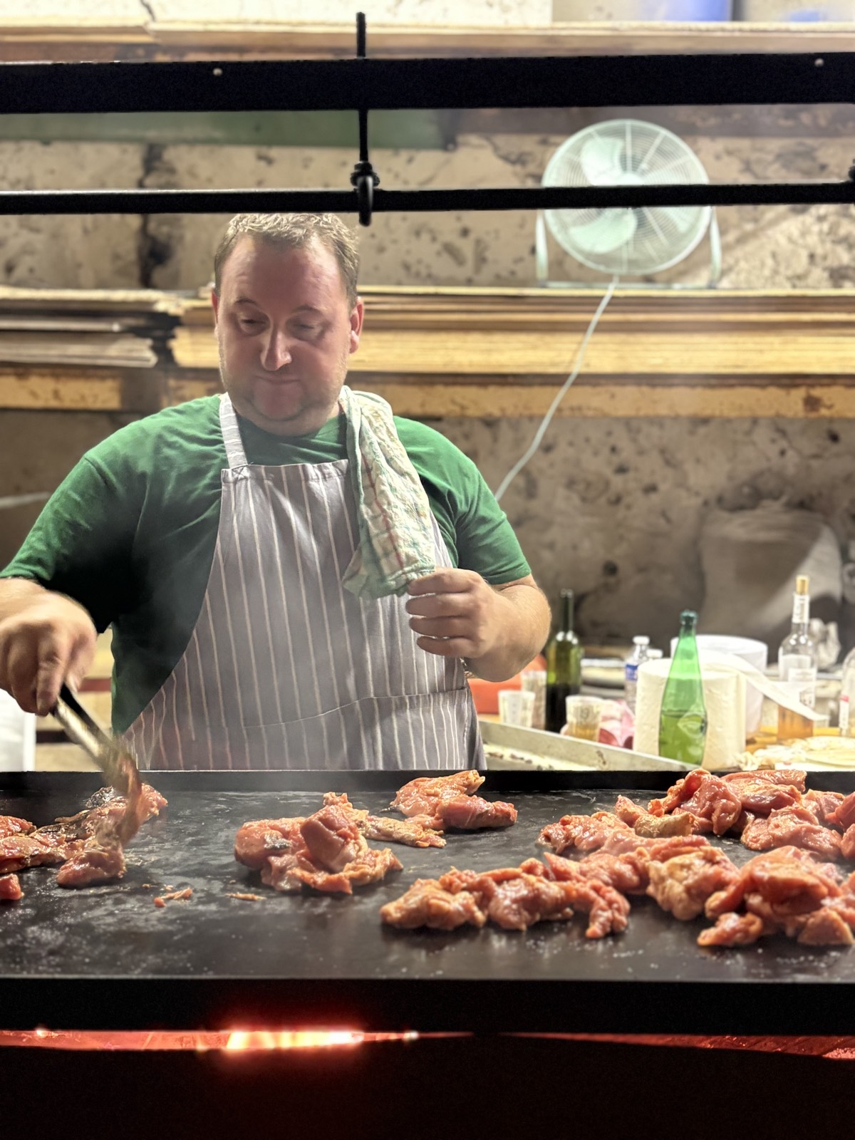 Un cuisinier en tablier dispose des morceaux de viande sur la plancha